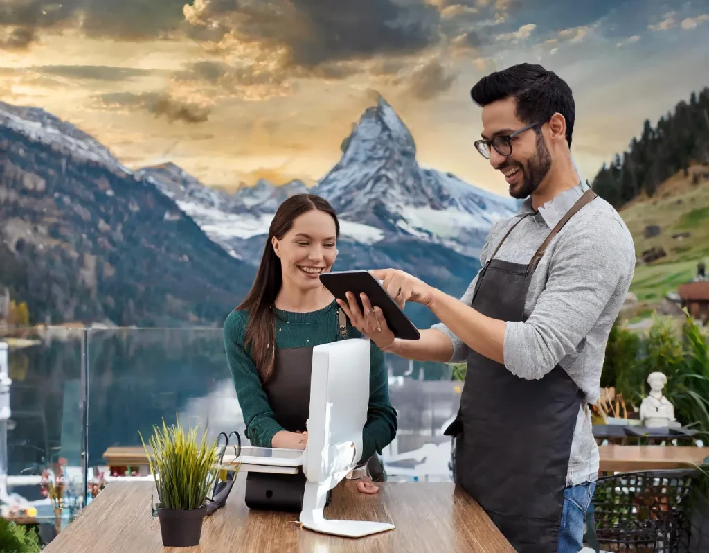 Smiling café employees use a tablet at a point of sale with a scenic mountain view in the background.